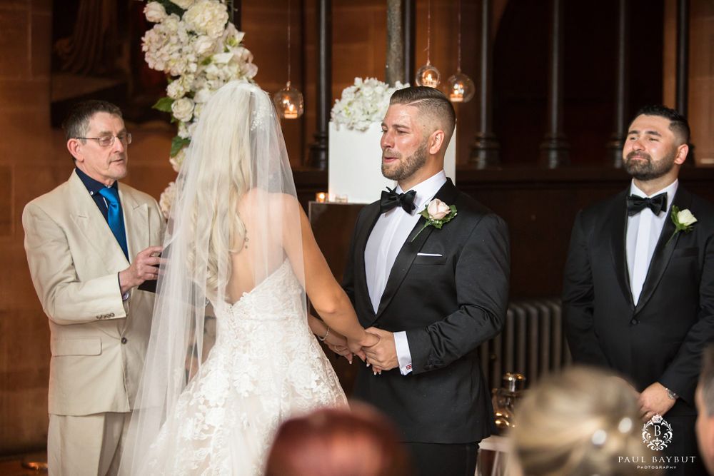 Wedding ceremony in progress with officiant in beige suit and white floral decor.
