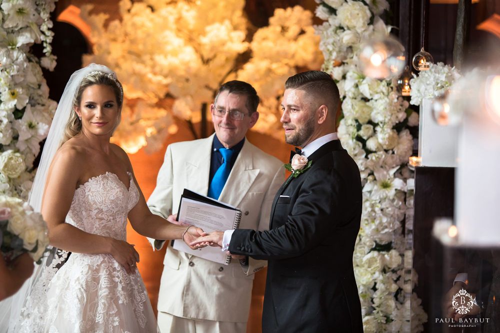 Elegant wedding ceremony with white floral archways and warm amber lighting.