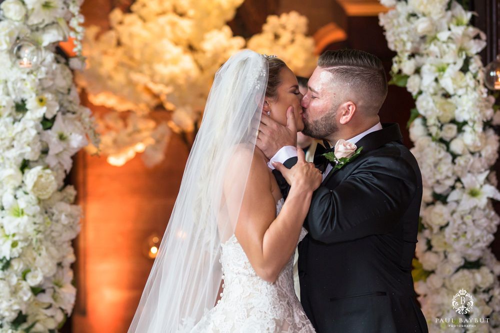 Romantic moment during wedding ceremony with white floral decor and warm lighting.