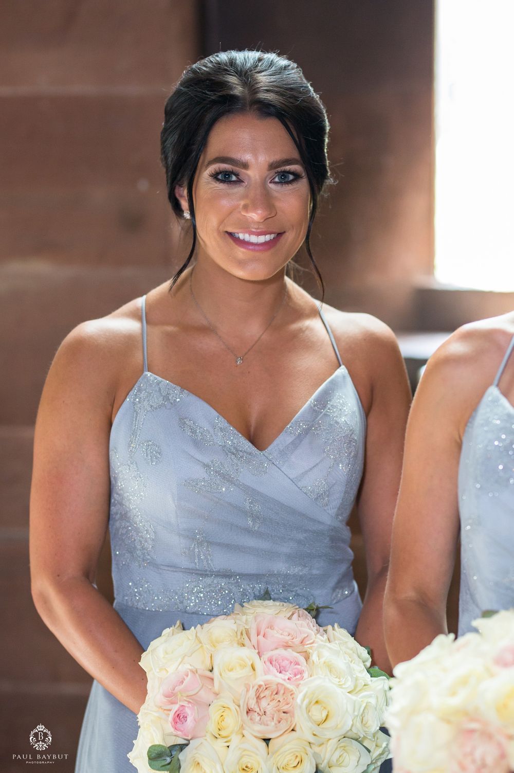 Bridesmaid in powder blue sparkly dress holds elegant bouquet of white and pink roses at wedding.