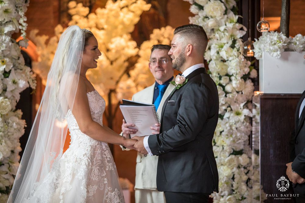 Wedding ceremony with elegant white floral archways and warm lighting as couple exchanges vows.