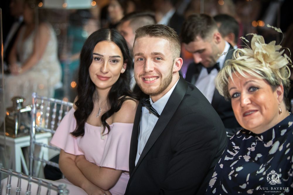 Wedding guests in formal attire smile together during reception celebration.