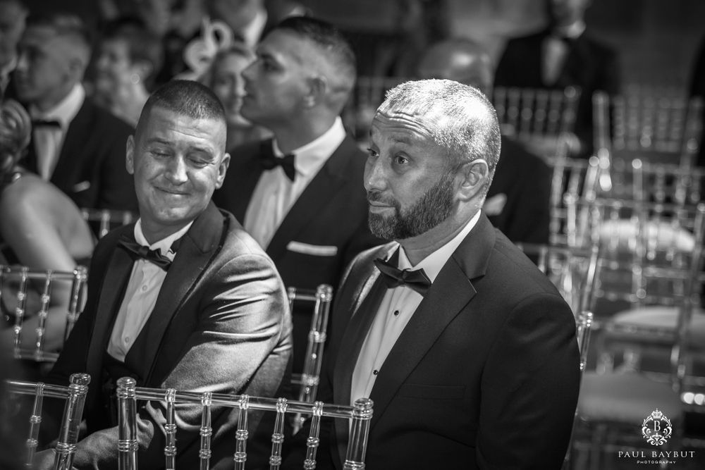 Two wedding guests in tuxedos chat during formal reception.
