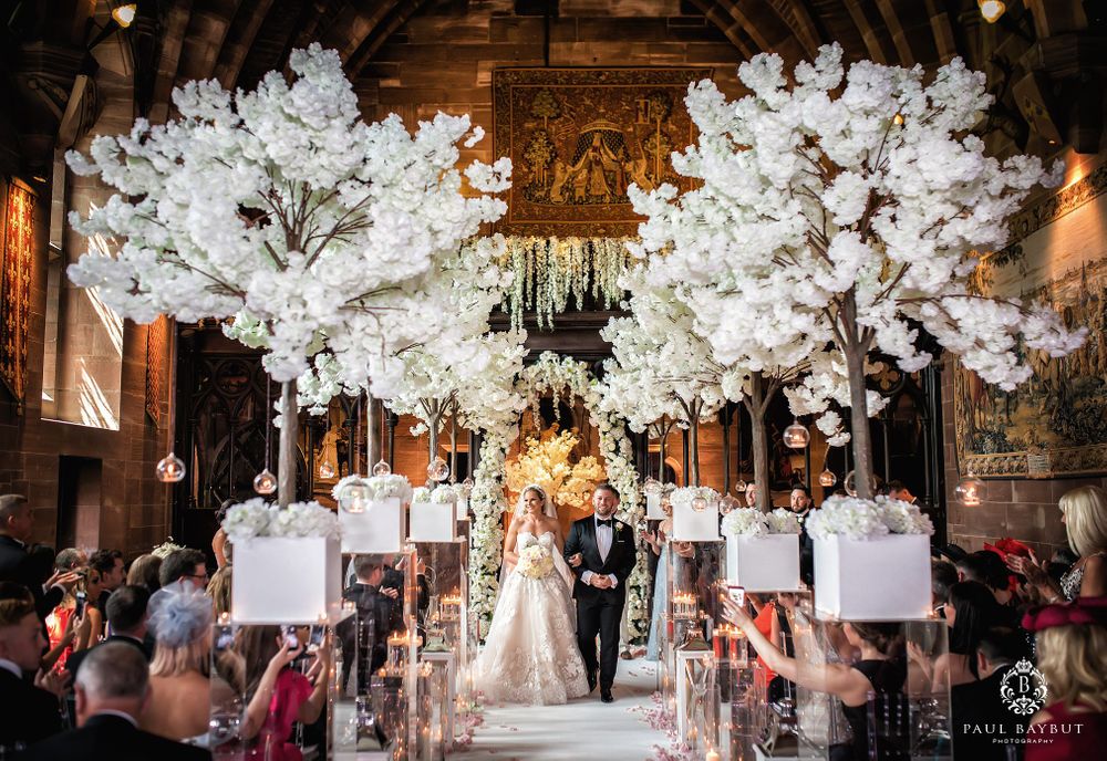 Wedding processional in wood-paneled venue with dramatic white cherry blossom trees lining the aisle.