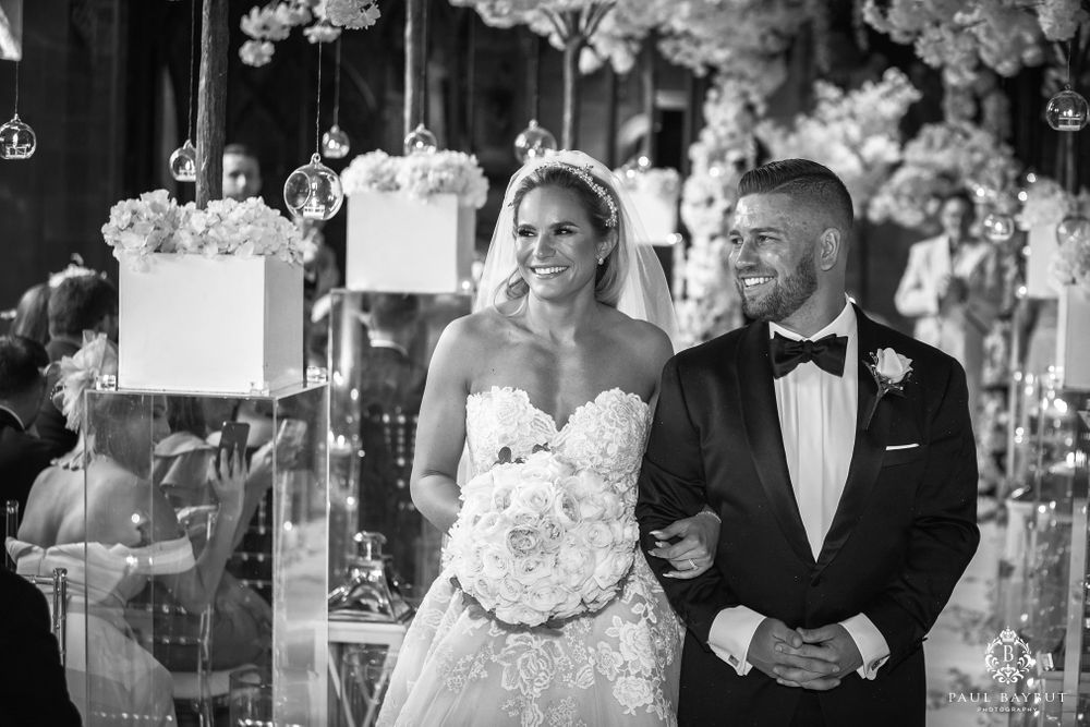 Newlyweds share joyful moment under white floral canopy during their wedding ceremony.