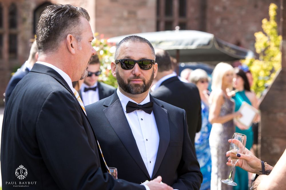 Two men in tuxedos having conversation during outdoor wedding reception.