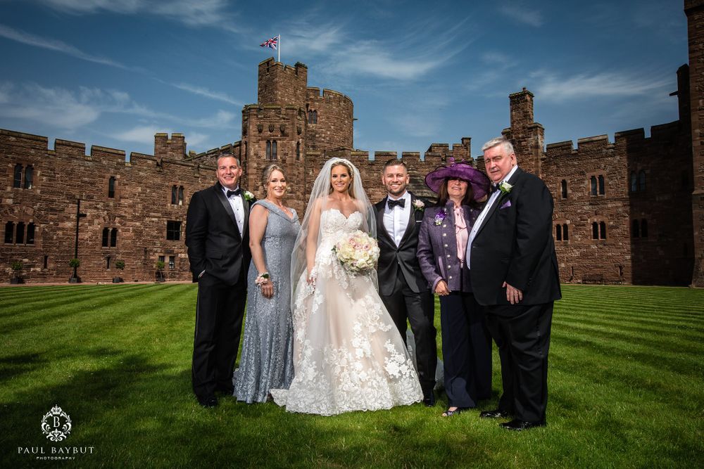 Wedding party members gather for a formal portrait on the castle lawn under blue skies.