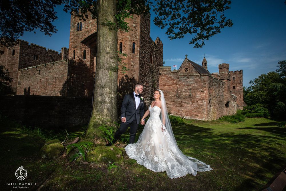 Romantic castle wedding portrait with couple standing beside ancient stone walls and tree.