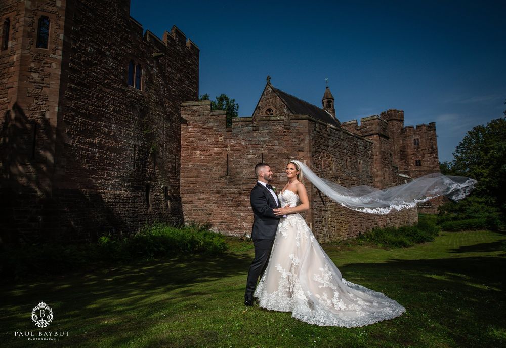 Castle wedding portrait with bride's veil flowing in breeze against stone fortress walls.