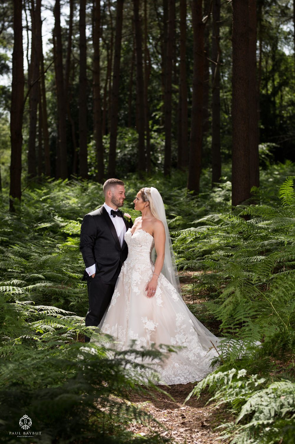 Romantic wedding portrait in enchanted forest setting surrounded by tall trees and ferns.