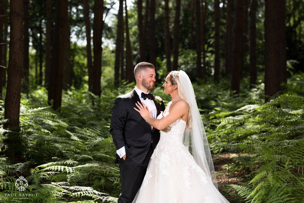 A romantic wedding portrait of a couple posing together amidst vibrant green ferns in a forest.