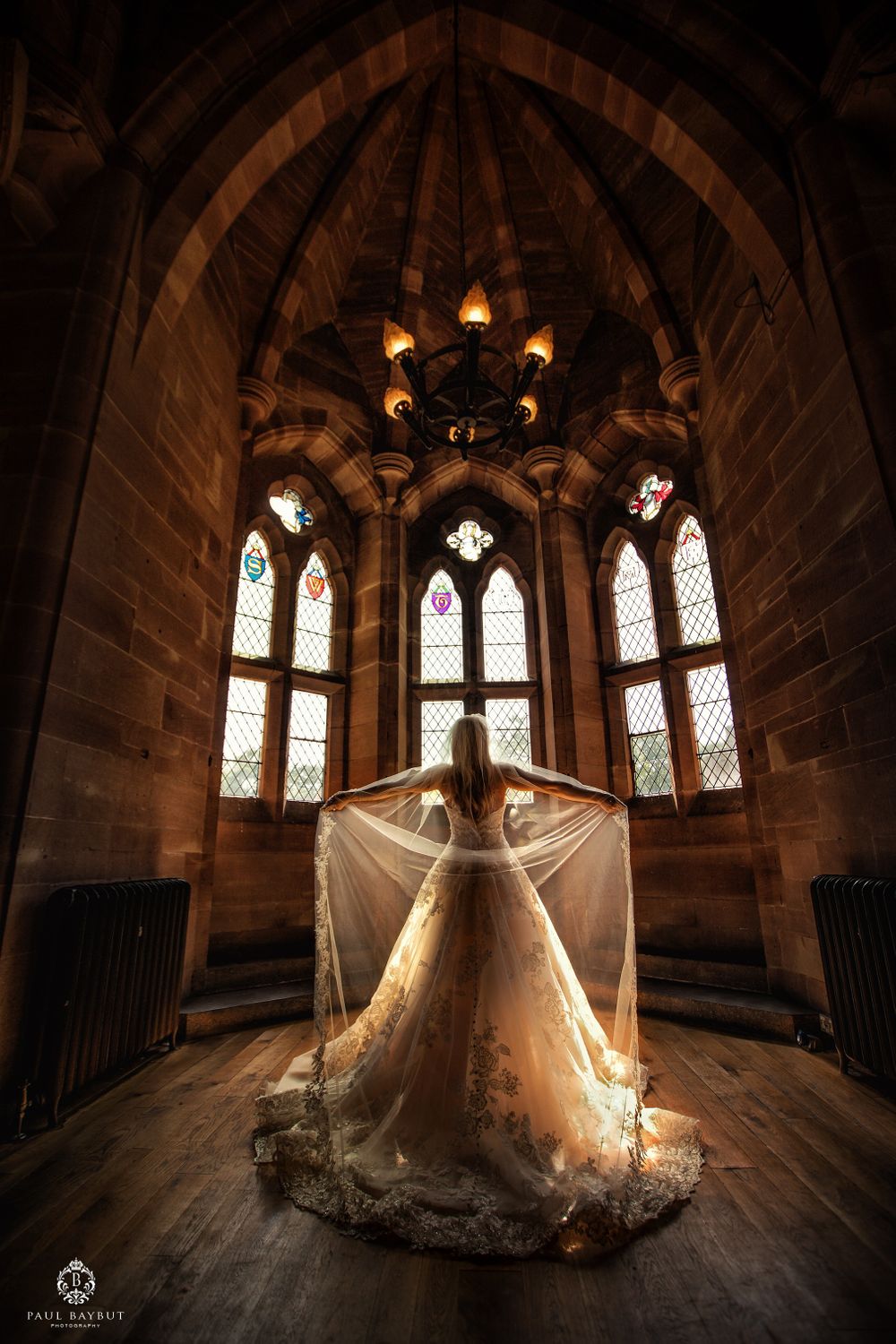 A flowing wedding dress and veil captured in dramatic lighting within a gothic chapel with stained glass windows.
