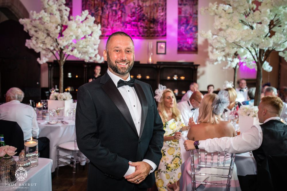 Elegant wedding reception venue decorated with white cherry blossom trees and purple accent lighting.