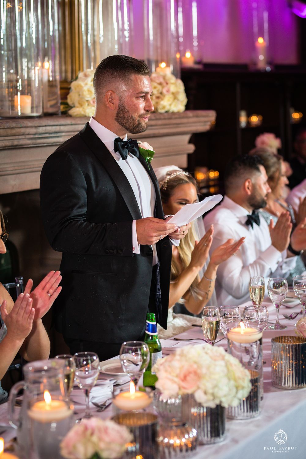 Wedding reception speech moment with candlelit tables and crystal chandelier decor.