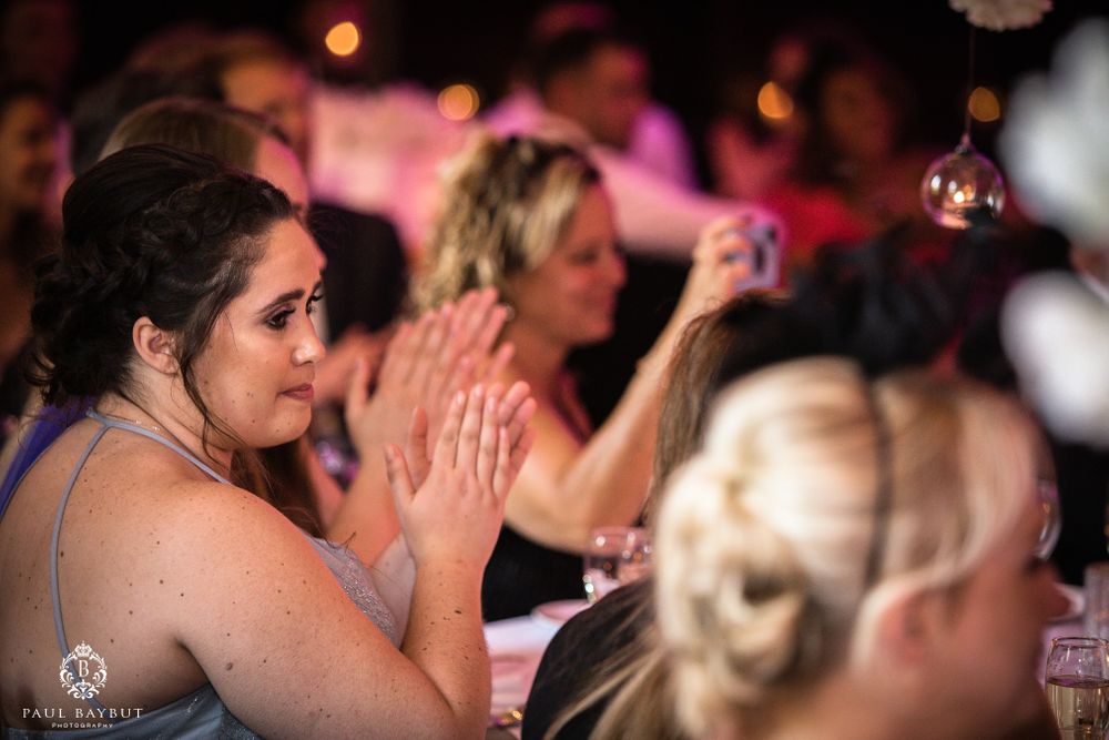 Wedding guests applauding during reception celebration with pink ambient lighting.