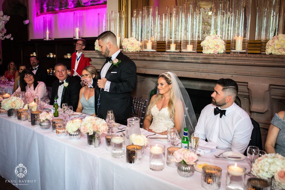 Wedding party seated at elegant head table with pink uplighting and floral centerpieces.