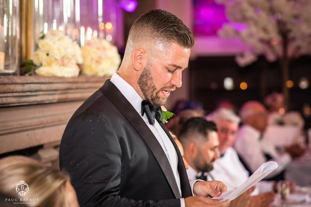 A speaker reads from papers during a wedding reception with purple ambient lighting and decorative elements.