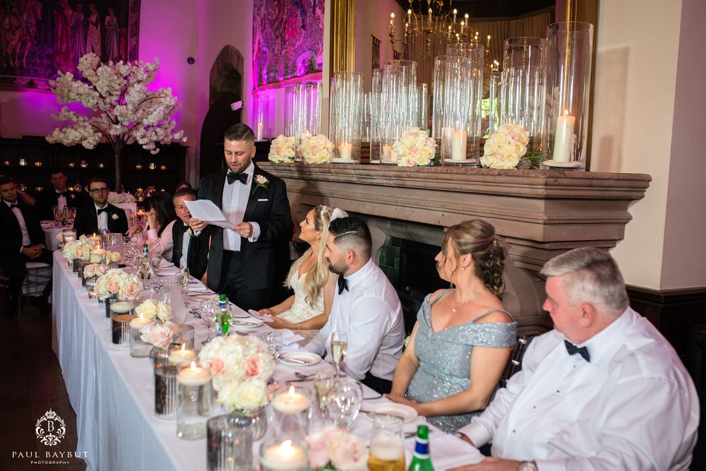 An elegant wedding reception table setting with candles, flowers and guests during evening speeches.