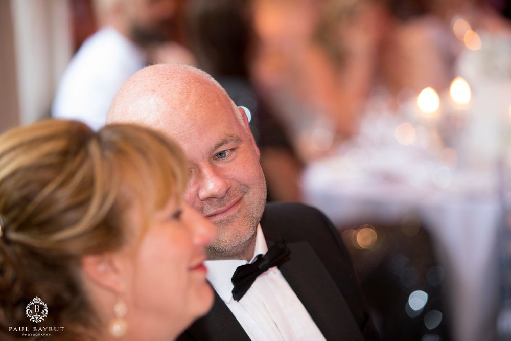 Guests share a joyful moment during wedding reception speeches with ambient lighting.