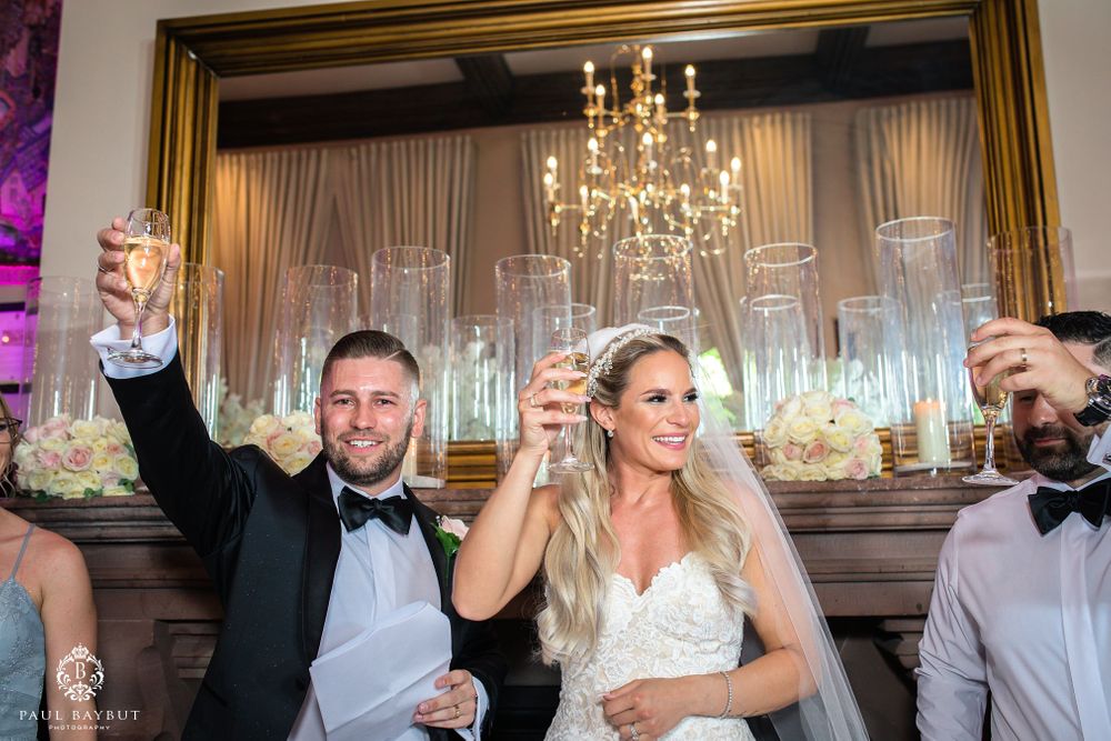 Wedding guests raise their champagne glasses for a celebratory toast under an elegant crystal chandelier.