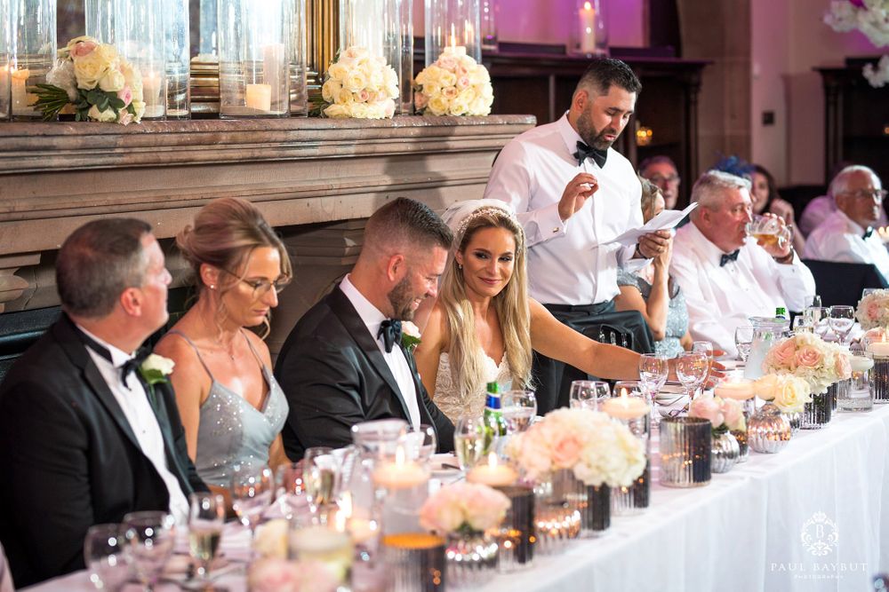 Wedding party seated at an elegant head table with floral centerpieces and pink uplighting.