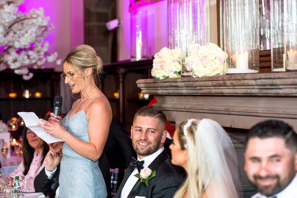 Wedding speech being delivered during reception with elegant floral decorations and pink lighting.