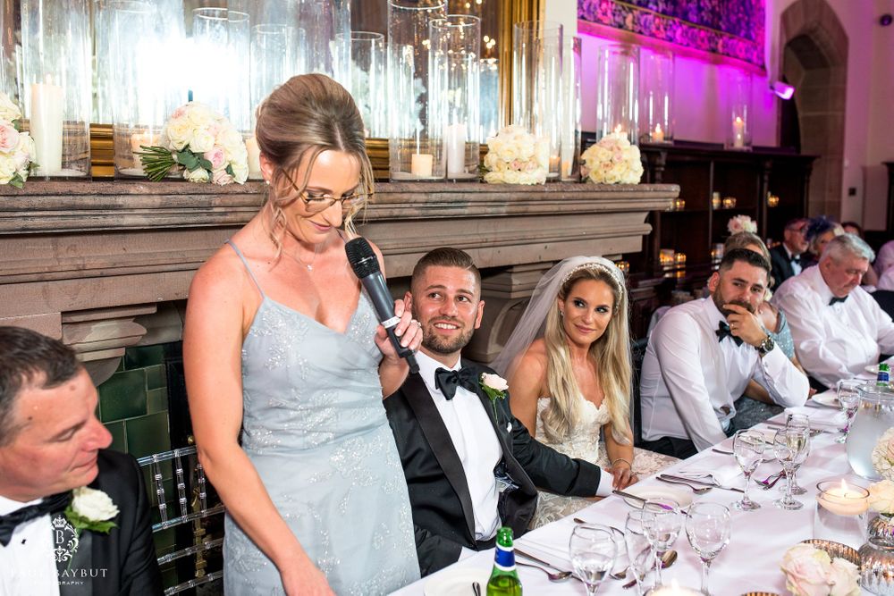 Wedding party seated at head table during reception with elegant decor and pink lighting.