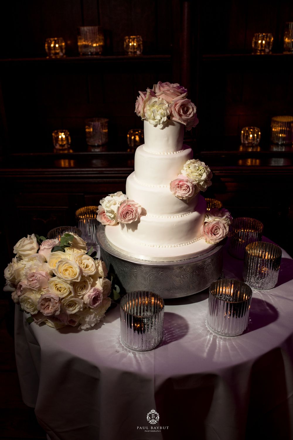 Elegant white wedding cake decorated with pink and white roses on a table with glowing candle holders.