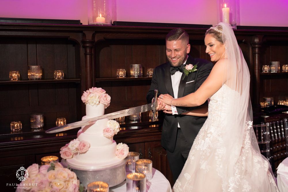 Newlyweds cutting their wedding cake together at reception with pink lighting.