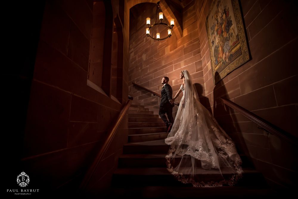A bride in a flowing white gown descends an elegant stone staircase in dramatic lighting with trailing veil.