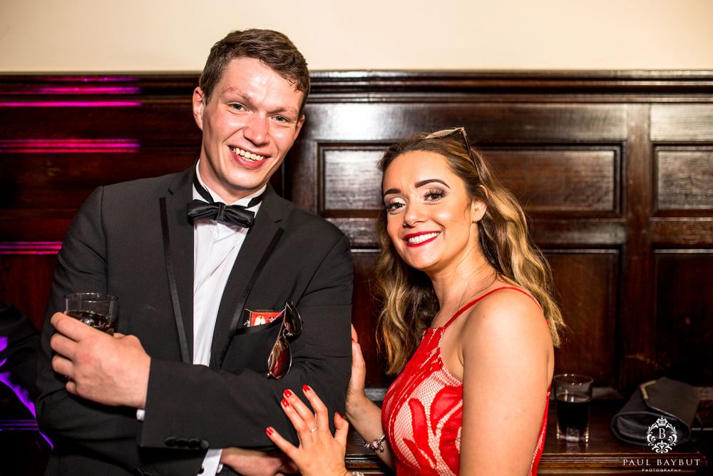 Wedding guests in formal attire laugh and celebrate during an evening reception.
