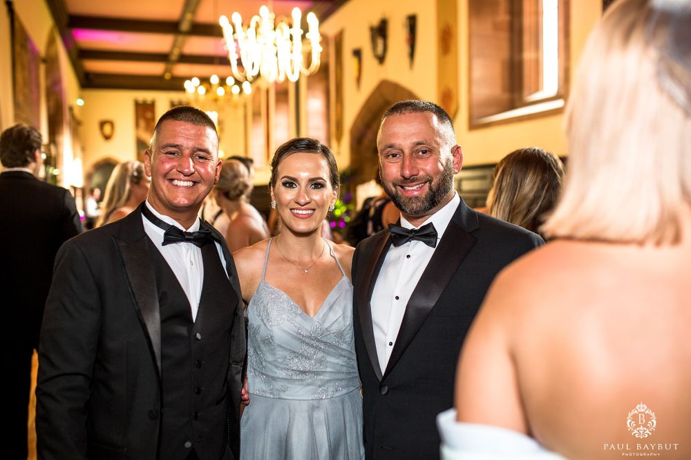 Guests in formal attire gather and smile during an elegant indoor reception with chandelier lighting.