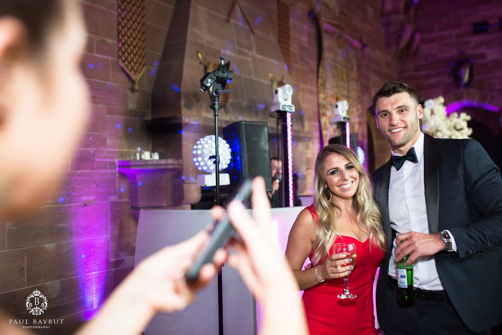 Guests in formal attire pose for photos during the wedding reception with purple lighting.