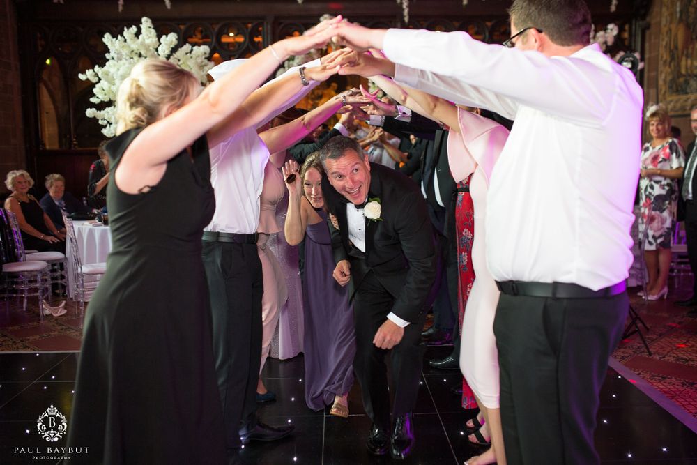 Wedding guests form a dancing circle with raised arms during the reception celebration.