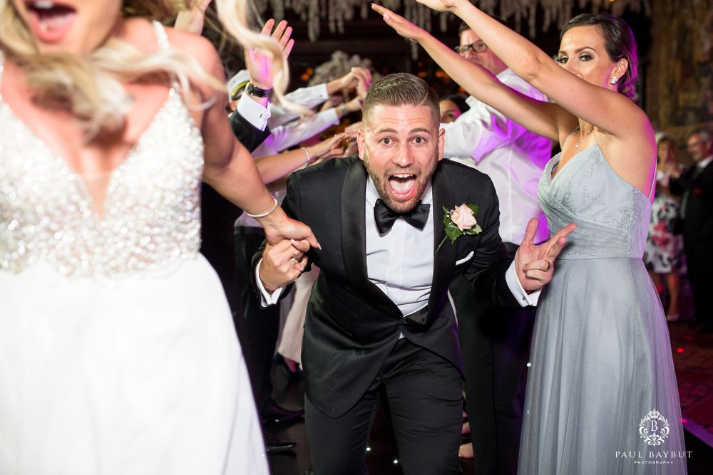 Lively wedding reception dance moment with guests reaching out under elegant hanging decor.