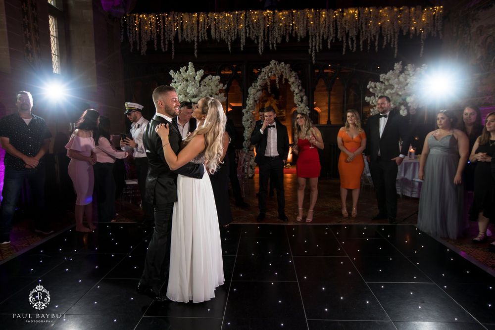 Wedding reception dance scene on black glittery floor with hanging floral decor and dramatic lighting.