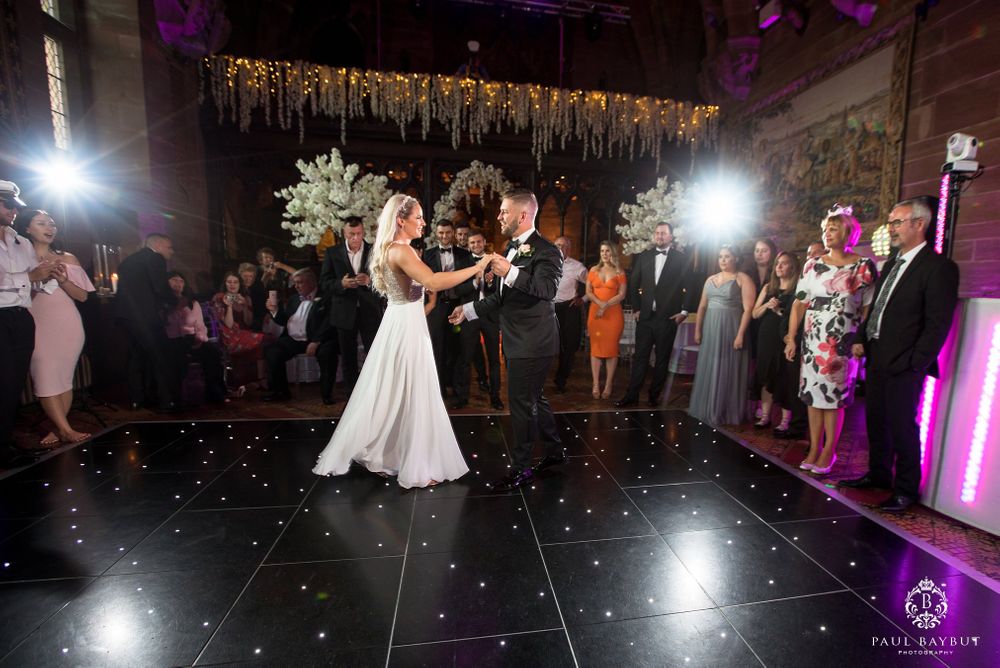 Wedding couple dancing on sparkly black floor under golden hanging decor with guests watching.