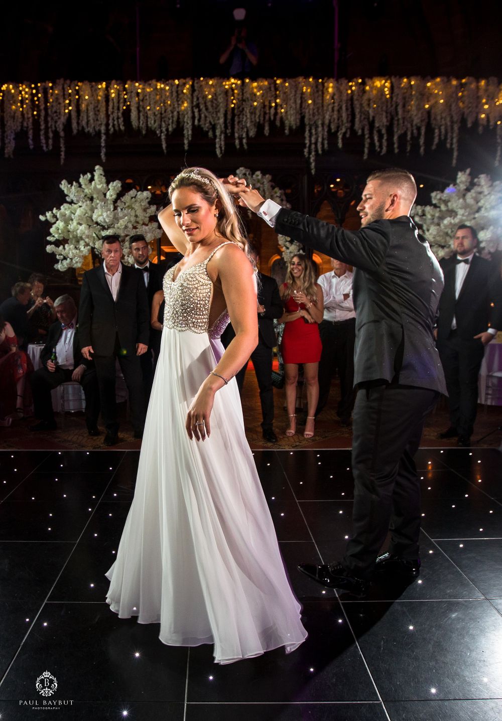 Elegant dance scene on black tile floor under hanging golden decor at wedding reception.