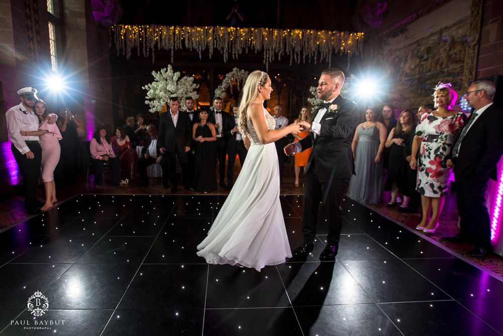 A couple shares their first dance on an illuminated black dance floor under hanging decorations at their wedding reception.