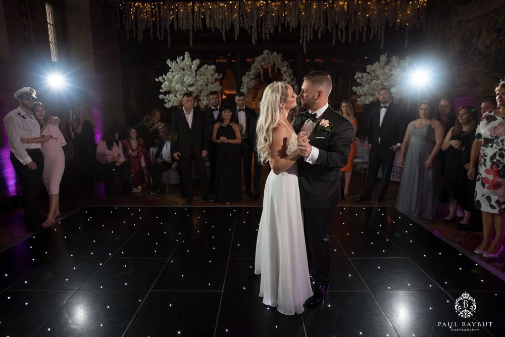 A couple dances intimately on a starlit black dance floor surrounded by wedding guests.