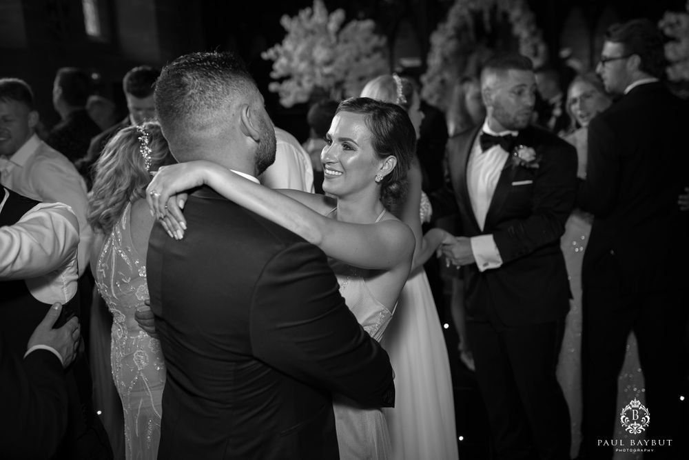 Dancing couples embrace on the wedding reception dance floor in black and white.