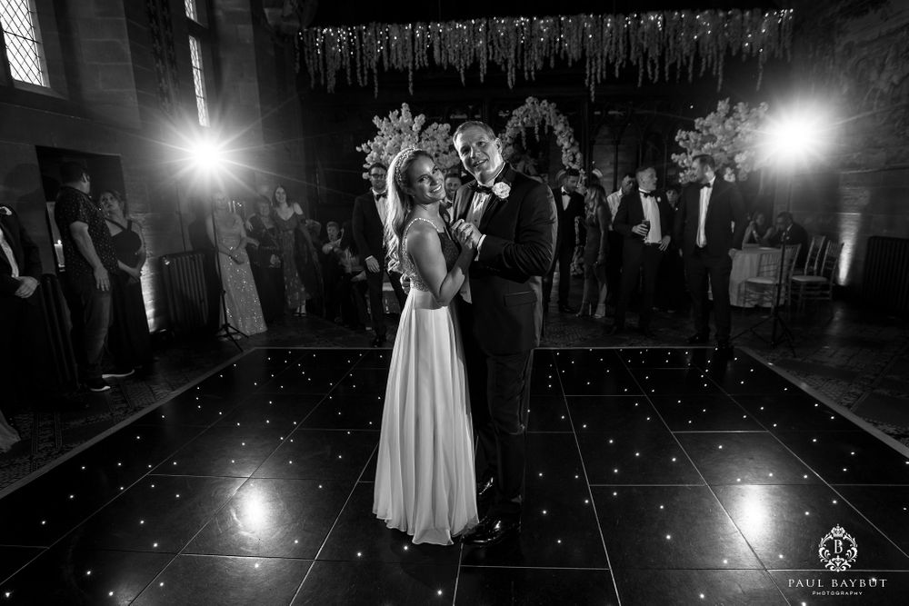A couple shares a romantic dance on an illuminated floor beneath shimmering ceiling decorations.