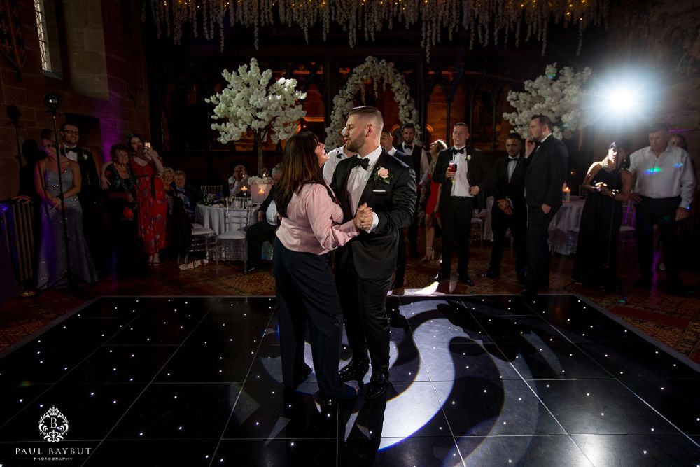 Romantic dance moment captured at wedding reception on black illuminated dance floor with decorative lighting.