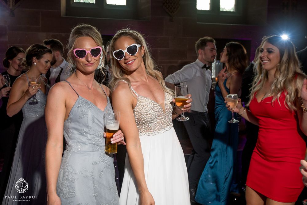 Wedding guests in sunglasses celebrate on the dance floor during an indoor reception party.