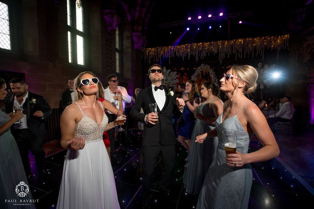 Wedding party dancing and celebrating at a dimly lit indoor venue with purple lighting.