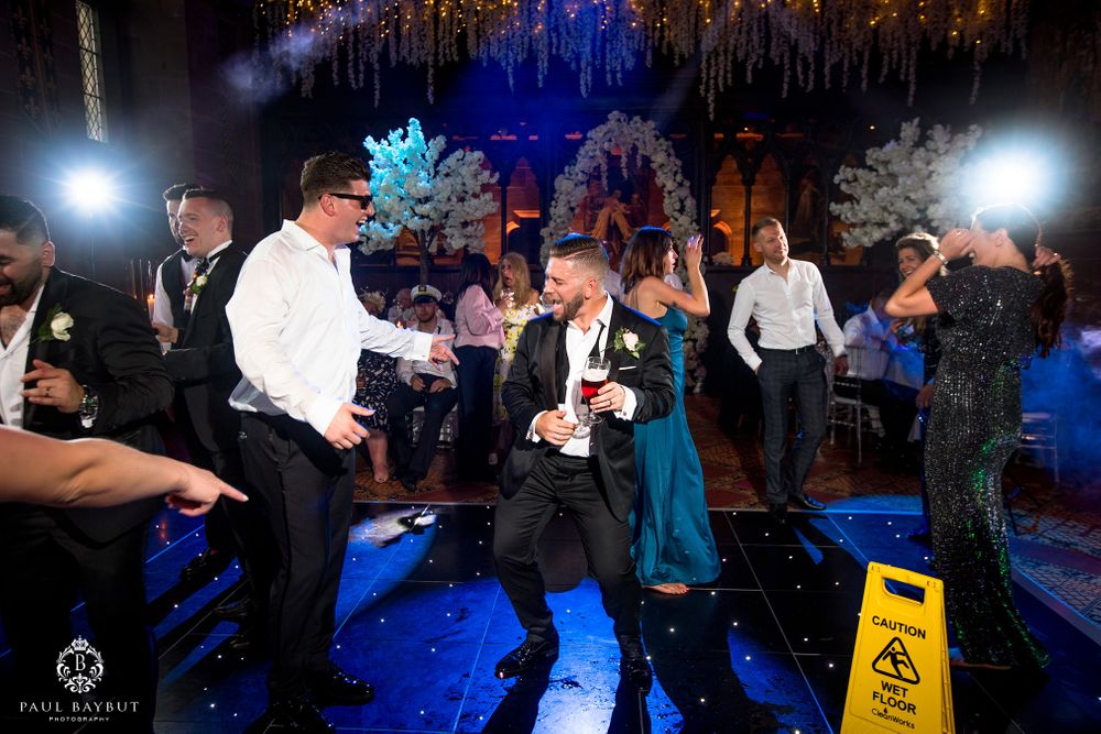 Wedding reception guests dancing enthusiastically under blue lighting on crowded dance floor.