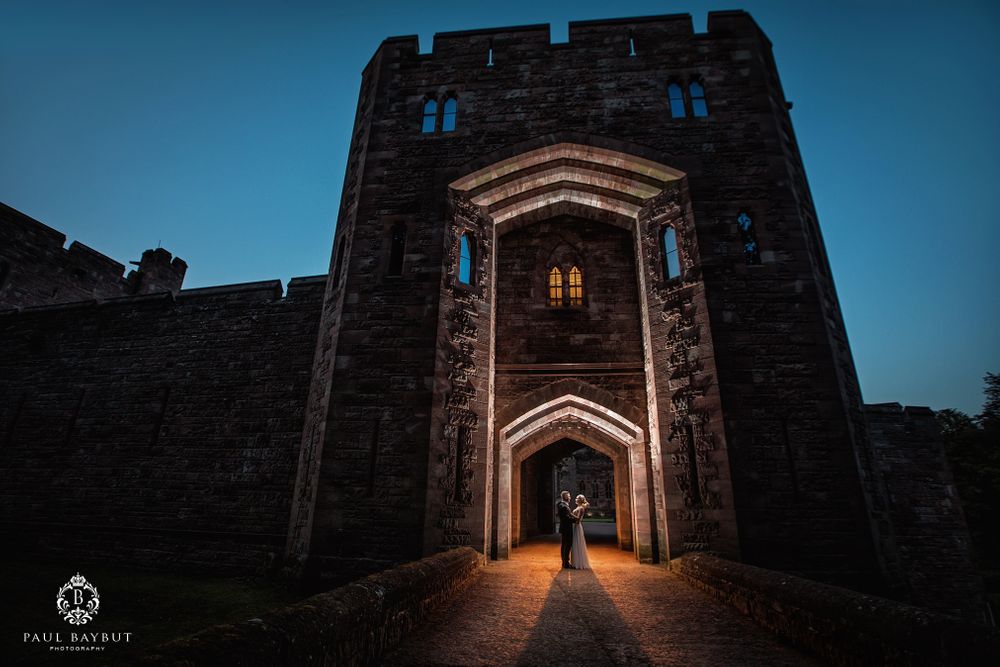 Dramatic twilight silhouette of couple in castle archway with illuminated windows.