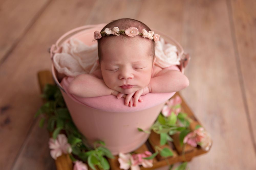 Sleeping newborn posed in pink bowl with floral decorations.