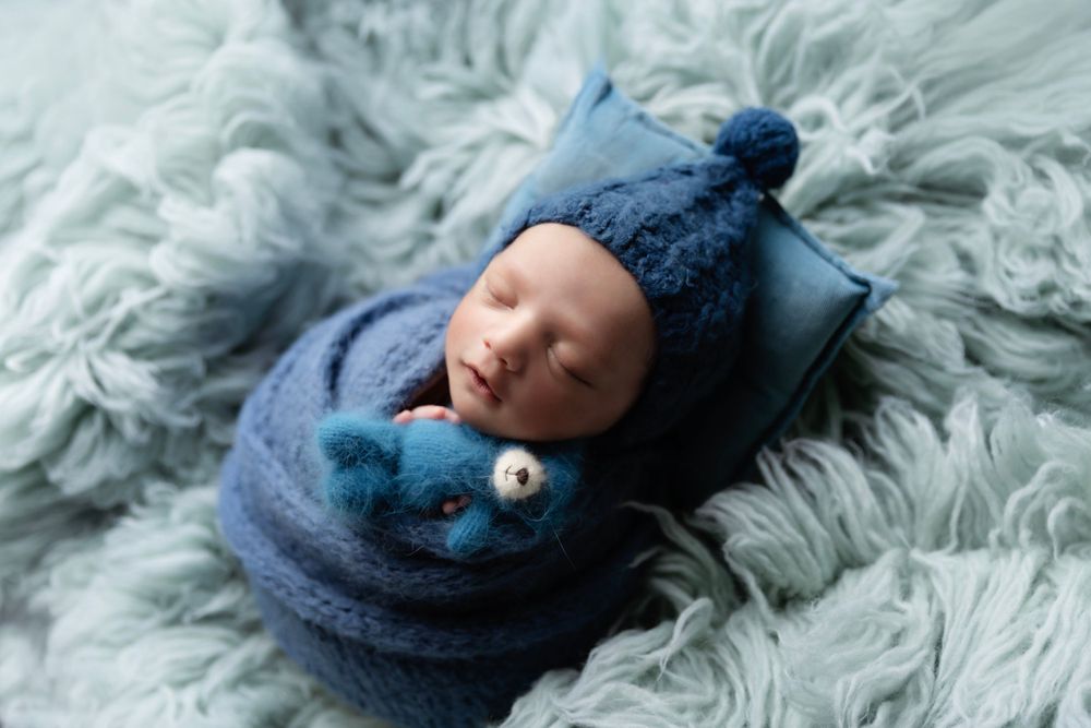 Sleeping newborn in blue winter outfit lying on soft blue-gray textured blanket.
