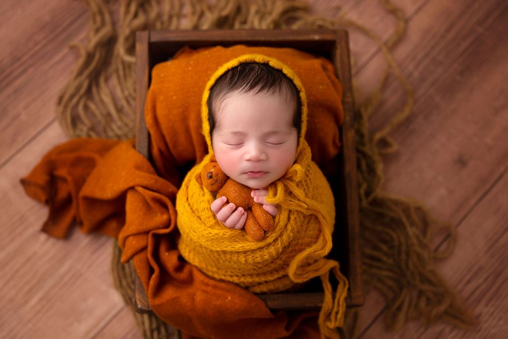 Sleeping newborn wrapped in golden knit blanket on wooden backdrop.